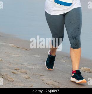 Ein Läufer in Grau Leggings ist ein Rennen auf dem harten Sand durch die Esser am Strand. Stockfoto