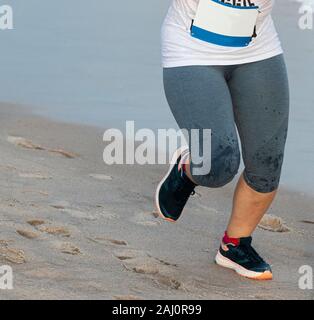 Ein Weibchen ist Joggen am Wasser auf dem harten Sand während eines Rennens am Strand. Stockfoto