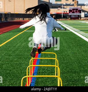 High School Jugendmädchen über zwei Fuß gelb hurldes, die auf einem grünen Rasen Feld während der Leichtathletik Praxis springen. Stockfoto