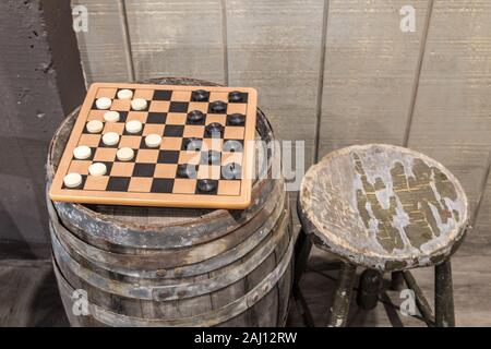 Altmodisches Spiel der Kontrolleure. Schachbrettmuster Spiel mit Steine auf einem alten hölzernen Keg Fass mit altem Holz Hocker. Stockfoto