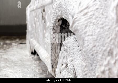 Ein Auto von Seife Schaum bedeckt beim Waschen in Innenräumen - close-up mit selektiven Fokus. Stockfoto