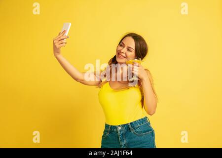 Die selfie, Vlog, lächelnd. Der kaukasische Frau Porträt auf Gelb studio Hintergrund. Schöne weibliche Modell. Konzept der menschlichen Gefühle, Mimik, Vertrieb, Ad. Sommer, Reisen, Resort. Stockfoto