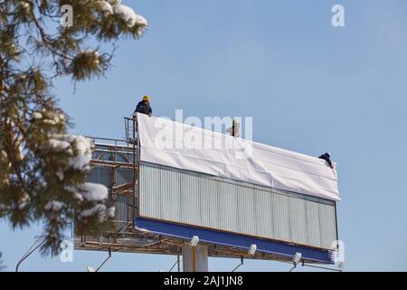 Arbeiter bereitet Billboard zum Einbau neuer Werbung. Industriekletterer arbeiten auf einer Leiter - die Platzierung eines Werbebanners. Stockfoto