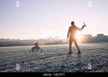 Frostigen morgen mit Hund. Junger Mann mit seinem Hund gegen Stadtbild bei Sonnenaufgang. Stockfoto