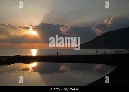 Wundervoller Sonnenaufgang, Sonnenstrahlen und Touristen am Strand von Adrasan Provinz Antalya in der Türkei. Es gab einen kleinen Teich am Strand mit Reflexionen. Stockfoto