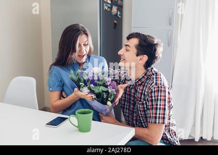 Mann gifting Blumenstrauß zu seiner Freundin auf Küche zu Hause. Valentines Tag romantische Überraschung. Glückliches Paar in der Liebe Stockfoto