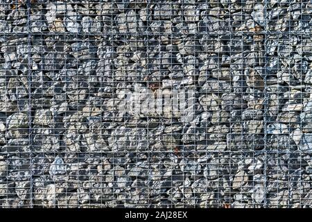 Gabionen Stützmauer Textur. Drahtgitter voll der rohen Natursteine. Mauerwerk Fassade Detail. Schützende Barriere. Gestapelte graue Felsen in metallischen Käfig. Stockfoto