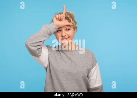 Ich bin Verlierer. Frustrierte Frau mit kurzen lockiges Haar in Sweatshirt mit lame oder Verlierer Geste mit L Finger auf Stirn, verärgert über Verlust des Arbeitsplatzes, failu Stockfoto