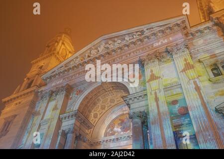 Budapest, Ungarn Weihnachtsmarkt am St Stephen Square mit animierten zeigen. Nachtansicht des Advents fest mit Laser visual auf Basilika Fassade projiziert. Stockfoto