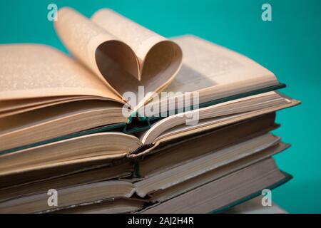 Stapel von Büchern auf Grün. herzförmige Buchseiten. Hintergrund Stockfoto