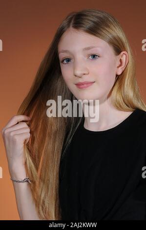 Hübsches blondes junges Mädchen mit schwarzen T-Shirt auf warmen Orange abgestuften Hintergrund Stockfoto