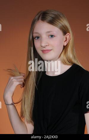 Hübsches blondes junges Mädchen mit schwarzen T-Shirt auf warmen Orange abgestuften Hintergrund Stockfoto