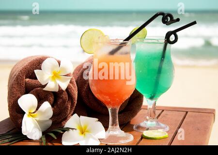 Tropische Eis im Sommer Drinks und Cocktails, Handtücher und ein Frauen Stroh Hut auf einem weißen Sandstrand auf einem Hintergrund von blauen Meer. Stockfoto