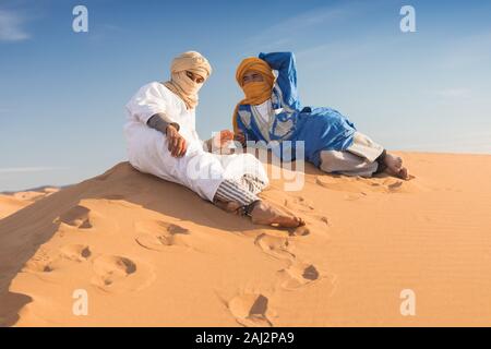 Porträt eines Beduinen Nomad mit bunten Turban und Lächeln sitzen auf Sand Dune in beliebten touristischen Ort Merzouga Wüste. Tuareg Mann Stockfoto