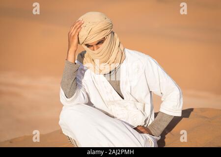 Porträt eines Beduinen Nomad mit bunten Turban und Lächeln sitzen auf Sand Dune in beliebten touristischen Ort Merzouga Wüste. Tuareg Mann Stockfoto