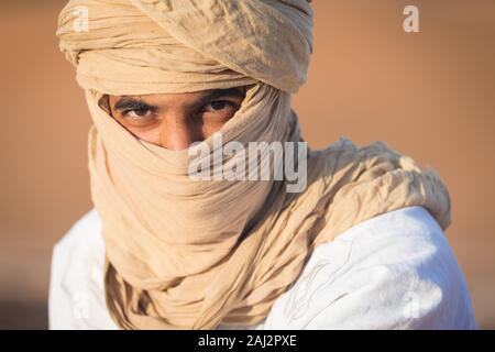 Porträt eines Beduinen Nomad mit bunten Turban und Lächeln sitzen auf Sand Dune in beliebten touristischen Ort Merzouga Wüste. Tuareg Mann Stockfoto