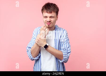 Handgelenk Schmerzen. Portrait von umgekippt braunhaarige Mann mit dem kleinen Bart und Schnurrbart in lässig-gestreiften Hemd seine verletzte Handgelenk grimassen von Schmerz, Stockfoto