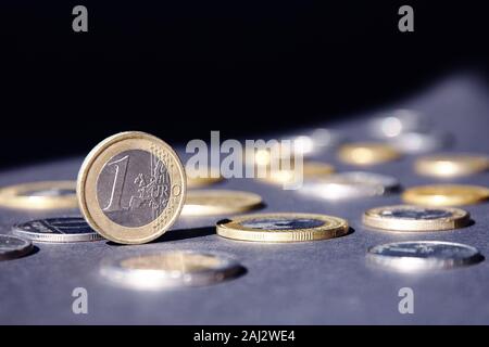 Ein Euro Münze auf der Kante shining in Spotlight, gegen viele verschiedene Münzen auf dunklem Hintergrund. Gelder fließen. Stockfoto