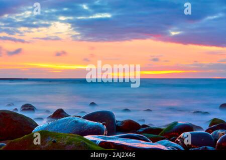 Sonnenuntergang über dem Meer und steinigen Strand mit Wasser in motion blur - Seascape. Lange Exposition Stockfoto