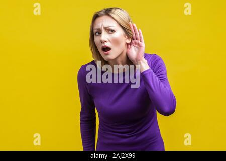 Ich kann nicht hören! Portrait von Neugierig aufmerksamen Frau in lila Kleid mit offenen Mund, Hand halten in der Nähe des Ohrs und sorgfältig geheim. Ich Stockfoto