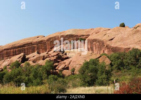 Große rote Felsformationen mit Bäume, Sträucher und Gräser wachsen auf und vor der Formationen auf der Trading Post Trail in Red Rocks State Park, Stockfoto