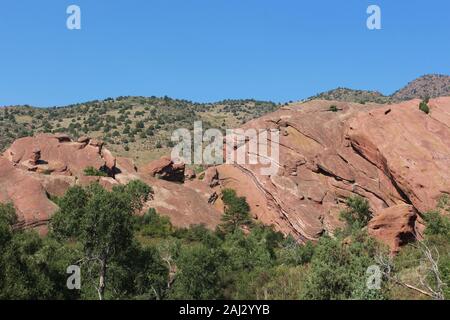 Große rote Felsformationen, ragt aus dem Boden, hinter Bäumen und Gräsern, auf der Trading Post Trail in Red Rocks State Park, Colorado, USA Stockfoto