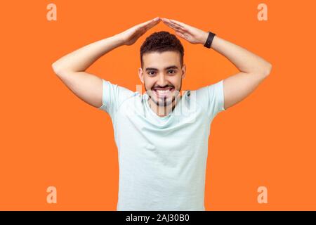 Ich bin sicher. Portrait von fröhlichen brünett Mann mit Bart und toothy Lächeln im casual weißes T-Shirt mit den Händen über den Kopf, so dass Dach Geste. Stockfoto