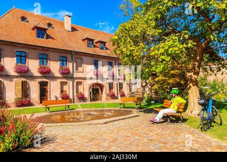 Junge Radfahrer sitzt auf der Bank vor der schönen Bergheim Rathaus, Elsass, Frankreich Stockfoto