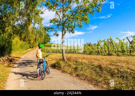 Junge Frau Radfahren auf der Straße entlang der Weinberge von Riquewihr in Hunawihr Dorf, Elsass, Frankreich Stockfoto