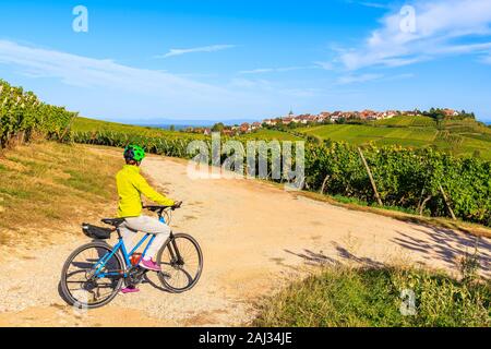 Junge Frau Radfahren auf der Straße entlang der Weinberge von Riquewihr in Hunawihr Dorf, Elsass, Frankreich Stockfoto