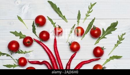 Kirschtomaten in der Nähe chili peppers als Dekoration. Essen für die Einrichtung. Tomaten in der Hälfte von pikanten Pfeffer auf grau Holz- Hintergrund. Vegetarische kunst Konzept. Stockfoto