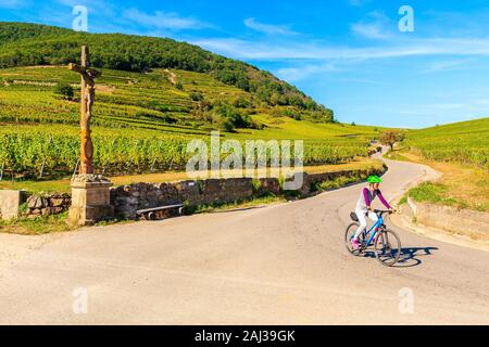 Junge Frau Radfahren auf der Straße entlang der Weinberge nach Kaysersberg, Elsass, Frankreich Stockfoto