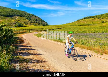 Junge Frau Radfahren auf der Straße entlang der Weinberge von Riquewihr, Kaysersberg, Elsass, Frankreich Stockfoto