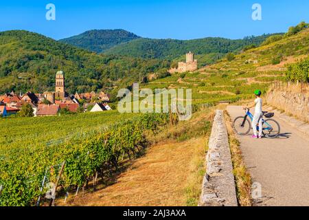 Junge Frau Radfahren auf der Straße entlang der Weinberge von Riquewihr, Kaysersberg, Elsass, Frankreich Stockfoto