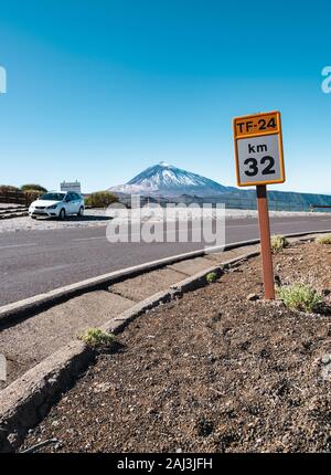 Km 32 der TF-24 Schild in den Nationalpark Teide auf Teneriffa mit einem geparkten Auto und den Berg Teide im Hintergrund. Stockfoto