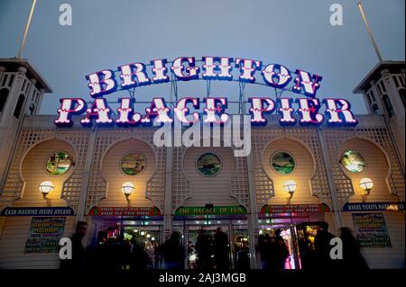 Das farbenfrohe, beleuchtete Schild des Brighton Palace Pier leuchtet in der Abenddämmerung. Der berühmte Pier in Brighton ist eine der beliebtesten Touristenattraktionen in Großbritannien. Stockfoto