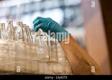 Eine Menge neues Bier Glas weiß leere Flaschen, kaukasische Mann mit blauen Gummihandschuh Holding eine Flasche, selektiven Fokus Nahaufnahme Stockfoto