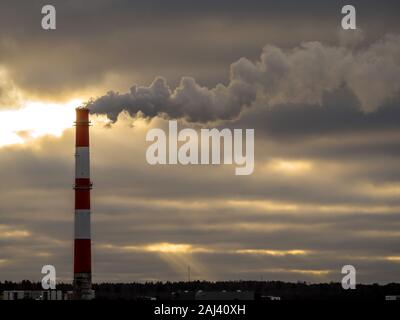 Stock Foto - Große industrielle rote und weiße Leitung mit Rauch von außen. Giftiger Rauch verschmutzt die Atmosphäre. Factory Leitung verschmutzen Luft, Umweltprobleme. Dunkle Wolken im Hintergrund. Toning Stockfoto