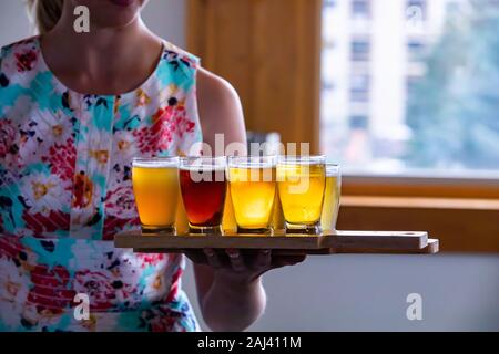 Selektiver Fokus auf Flug von Craft vier verschiedene Biere Gläser auf Holz- zwei Fach, einer weißen Frau, die die Fächer im Hintergrund Stockfoto