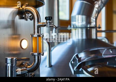 Schauglas voller goldener Bier auf Rohr aus Edelstahl mit Schlauch bib Hahn Ventil und tri Schellen selektiven Fokus, Brauerei Tanks und Behälter Hintergrund Stockfoto