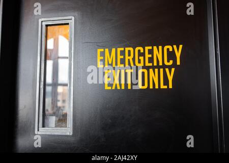 Notausgang nur Gelb Vinyl Sticker text Informationen Zeichen auf einem schwarzen Tür mit Glas, industrielle Zimmer Symbol, selektive konzentrieren und Ansicht schließen Stockfoto