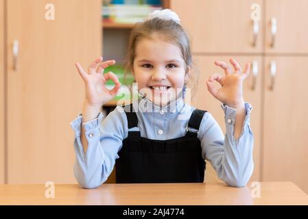 Mädchen Schülerin sitzt an ihrem Schreibtisch und zeigt die Zeichen in Ordnung. Stockfoto