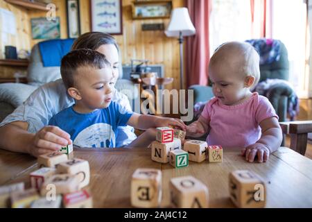 Mutter hilft ihren beiden Kindern, gut zusammen zu spielen. Stockfoto