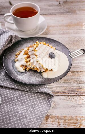 Vertikaler hausgemachte Waffeln mit Heidelbeeren und Eis und einer Tasse Tee. Nachtisch. Hausgemachte backen. Stockfoto