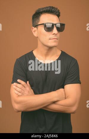 Studio shot von jungen hübschen Hispanic Mann mit schwarzen Hemd gegen braunen Hintergrund Stockfoto