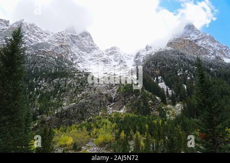 Ein Blick auf die Kaskade Canyon hoch aufragenden Wände mit schneebedeckten Gipfeln, herbstlichen Farben und einem Wasserfall. Stockfoto