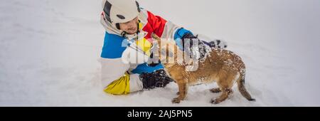 Junge männliche Snowboarder spielt mit Welpen bei einem Skigebiet im Winter BANNER, LANGE FORMAT Stockfoto