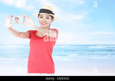 Asiatische Mädchen in hat die selfie Verwenden der Kamera Handy mit einem blauen Himmel im Hintergrund Stockfoto