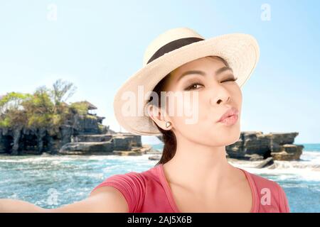 Asiatische Mädchen in hat einen selfie mit einem lustigen mit der Kamera Handy mit Tanah Lot Tempel Hintergrund Gesicht Stockfoto