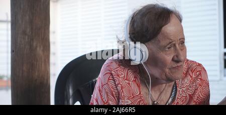 Ein Porträt einer alten Frau und Musik hören mit Kopfhörern im Freien genießen. Stockfoto